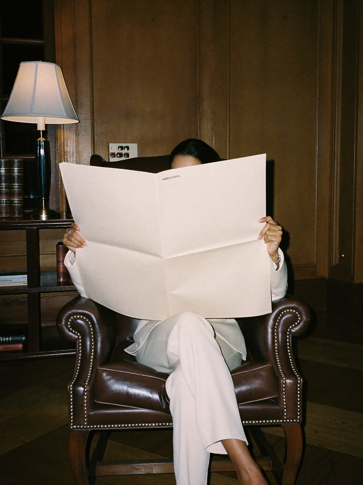 A woman in a leather armchair, the morning brief held up in front of her